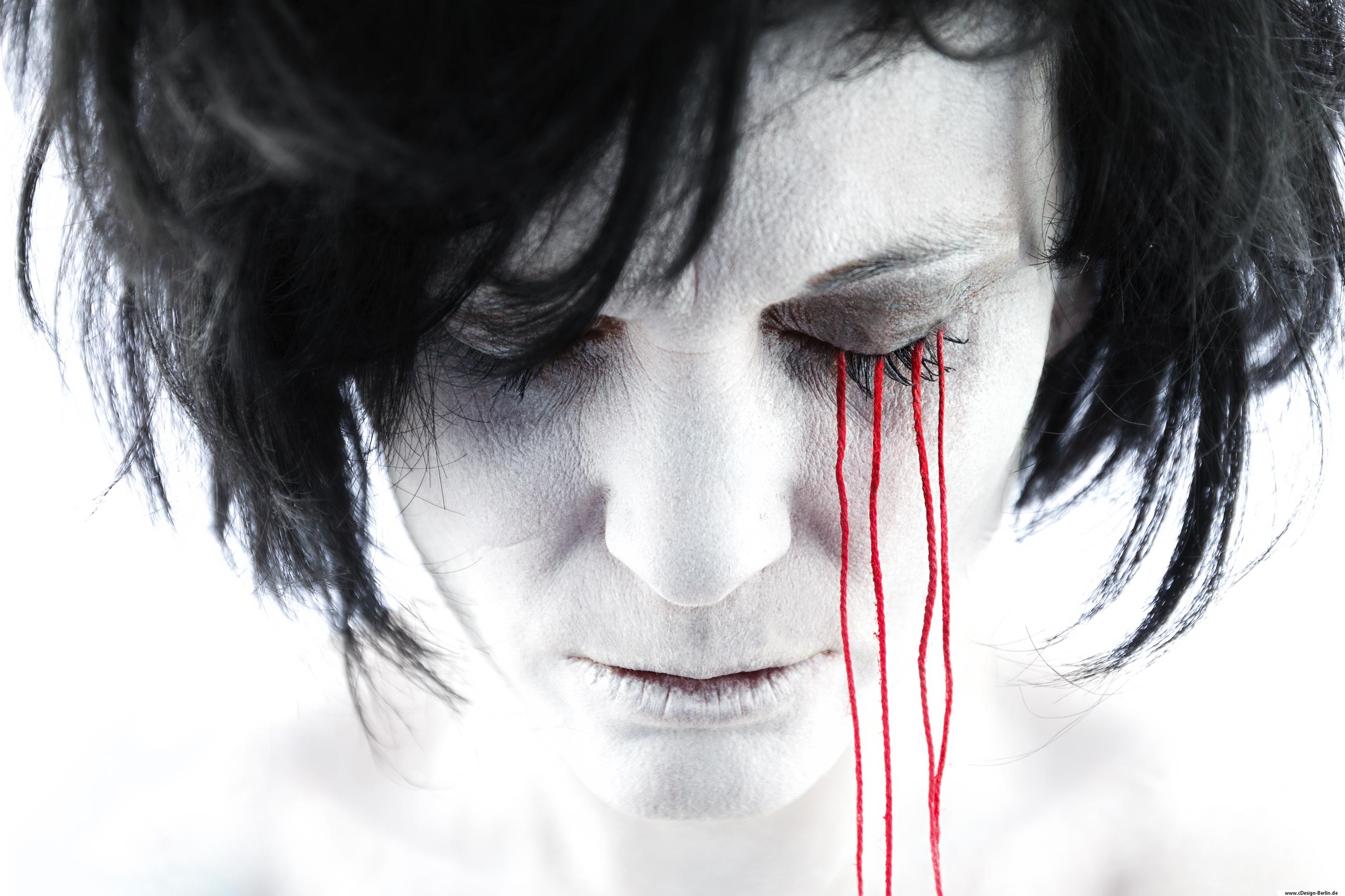 Fotografie ist Kunst und diese liegt bekanntlich im Auge des Betrachters. Auf diesem Foto sieht man eine Frau in Frontansicht, ihr Kopf leicht gesenkt, ihre Augen verschlossen. Ihr schwarzes Haar zerzaust, ihr Gesicht schneeweiß, ihr Mund leicht geöffnet. Von ihrem rechten Augenlid hängen lange rote Fäden herunter. Es sieht aus als ob sie schlafen würde. Das Gesamtbildnis ist hell gehalten, man spürt Kälte.