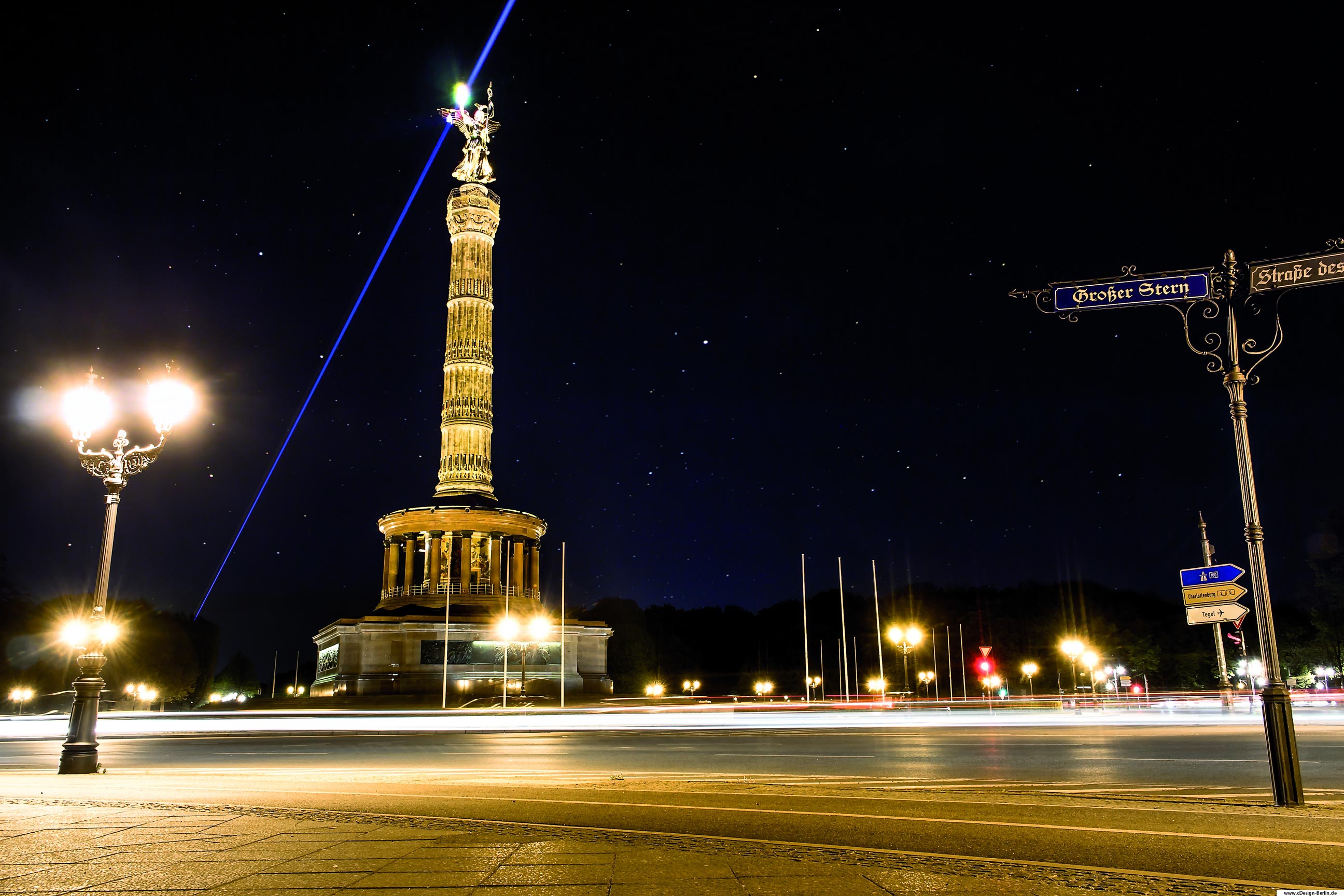 Die Siegesäule steht inmitten des Großen Tiergartens in Berlin. Sie steht unter Denkmalschutz und gilt neben dem Berliner Fernsehturm als Wahrzeichen von Berlin.Um sie herum führt ein Kreisverkehr und die Siegessäule selbst ist für jedermann zugänglich und kann bestiegen werden. Dieses Foto ist wieder in einer lauen Sommernacht entstanden. Berlin zu dieser Jahreszeit mit all seinen Lichtern ist einfach ein Traum. Mittig steht die Goldelse, wie sie liebevoll von den Berliner Bürgern genannt wird. Vor ihr der Kreisverkehr mit fahrenden Autos, die ich ebenfalls mit einer Langzeitbelichtung fotografiert habe. Ein blauer Laserstrahl von unten links strahlt die Figur an. Rechts vom Bild ist ein altes Straßenschild mit Verschnörkelungen zu sehen, dessen Richtung zum Großen Stern und zur Staße des 17.Junis zeigt. Bezirk: Berlin- Tiergarten
