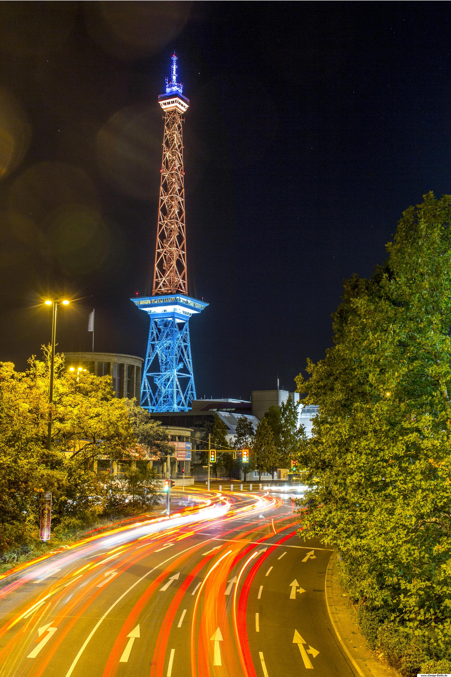 Das Messegelände liegt im Berliner Ortsteil Westend des Bezirks Charlottenburg- Wilmersdorf zwischen der Masurenallee, dem Messedamm, der Thüringer Allee und der Jaffestraße. Das bekannteste Objekt ist der Funkturm. Es zählt zu den bedeutendsten Bauwerken der deutschen Nachkriegszeit. Das Gelände ist vorallem für die Vielzahl abwechslungsreicher Ausstellungen bekannt. Die bekannteste ist wohl die Grüne Woche, um nur eine von ihnen zu bennenen. Dieses Foto ist in der Vogelperspektive in einer Berliner Nacht entstanden. Unter mir die Fahrbahn in Langzeitbelichtung, ein Meer voller Farben. Rechts und links vom Bild Bäume und mittig im Bild majestetisch der Funkturm zu sehen. Sein unteres Ende leuchtet blau und das obere Ende hat einen goldfarbenen Schimmer. Bezirk: Berlin- Charlottenburg- Wilmersdorf