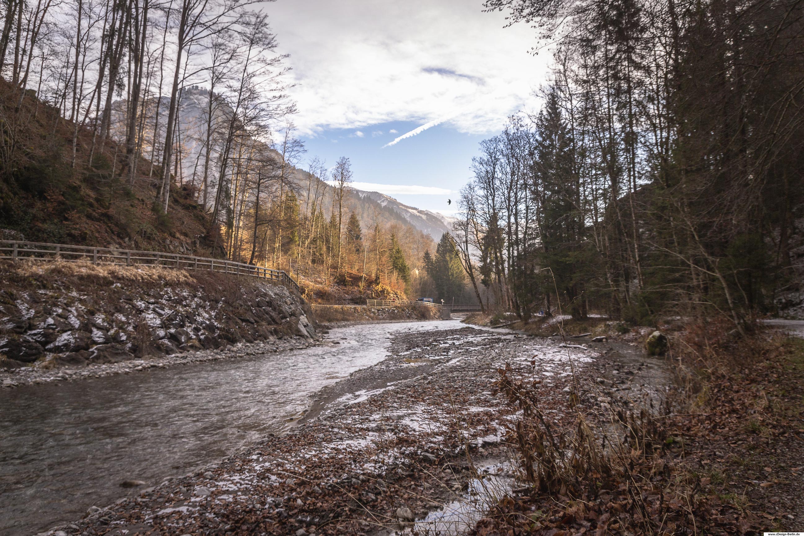 Stell dir vor du stehst mitten in einem Fluss, nicht zu flach und nicht zu tief. Links und Rechts befinden sich kleine Wege, umgeben von Wald. Vor dir in weiter Ferne, liegen die Berge mit ihren schneebeeckten Gipfeln. Über ihnen kreist ein Vogel. Die Wolken reißen auf und der Himmel zeigt sich im Azurblau. Die Sonnenstrahlen durchdringen den Wald und schenken der kalten Jahreszeit ihre Wärme.