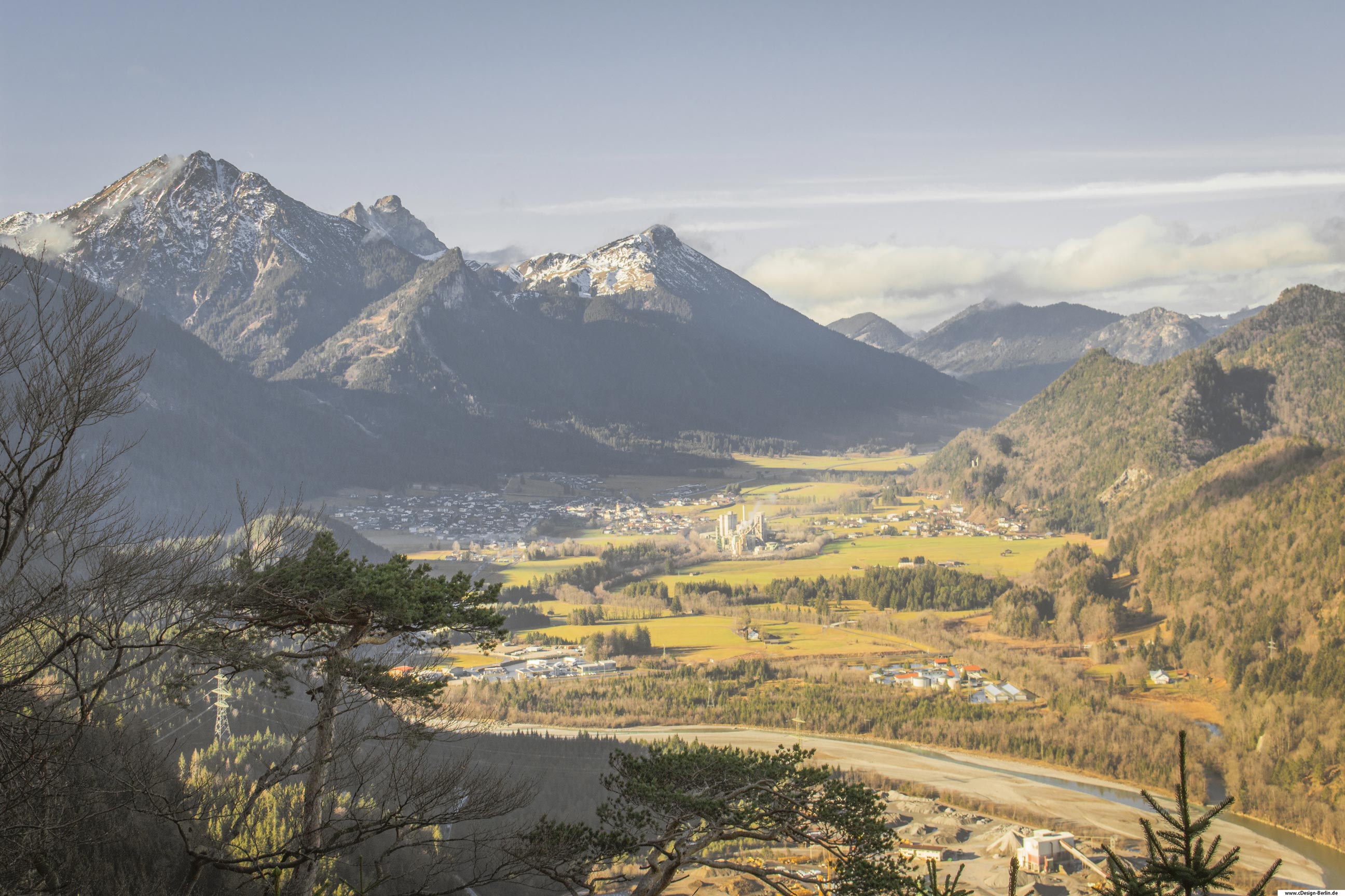 Auf diesem Bild schaue ich auf ein Tal hinab, welches von einem Fluss durchkreuzt wird. Rechts von dem Fluss liegt ein kleines Dorf. Dieses Dorf ist in Berge eingebettet. Die rechten Berge sind mit Bäumen bewachsen, erscheinen eher klein im Vergleich zu den linken Bergen, welche wie ein Fels in der Brandung in den Himmel empor ragen. Auch ihre Gipfel sind weiß gepudert. Man möchte meinen die Berge beschützen die Bewohner des Tales, geben ihnen Sicherheit und Fieden. Weiter am Horizont befinden sich ebenfalls Berge deren Gipfel von einer Wolkendecke umhüllt sind. Das Dorf befindet sich im Dreiländereck Österreichs.