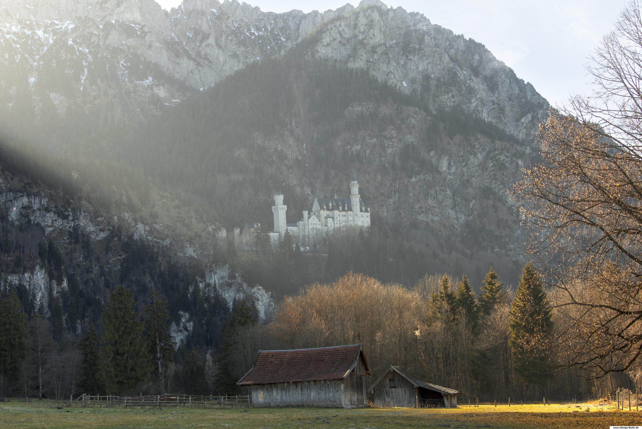 Ich stehe auf einer Wiese, vor mir eine alte, große und kleine Scheune. Links hinter der Großen Scheune ein Holzzaun, darin ist leicht ein Futtertrog zu erkennen. Ein großer Lichtsrahl zieht sich von links nach rechts auf die kleine Scheune in diesem Bild. Vor der Scheune rechts im Bild befindet sich ein großer Baum , der zur Hälfte abgebildet ist. Hinter den Scheunen Wald. Über dem Wald sind die Berge und in ihnen ein weißes Schloss eingebettet, welches an ein Märchen erinnert. Es beschreibt die Kluft zwischen arm und reich und die zwei Welten die aufeinander treffen.