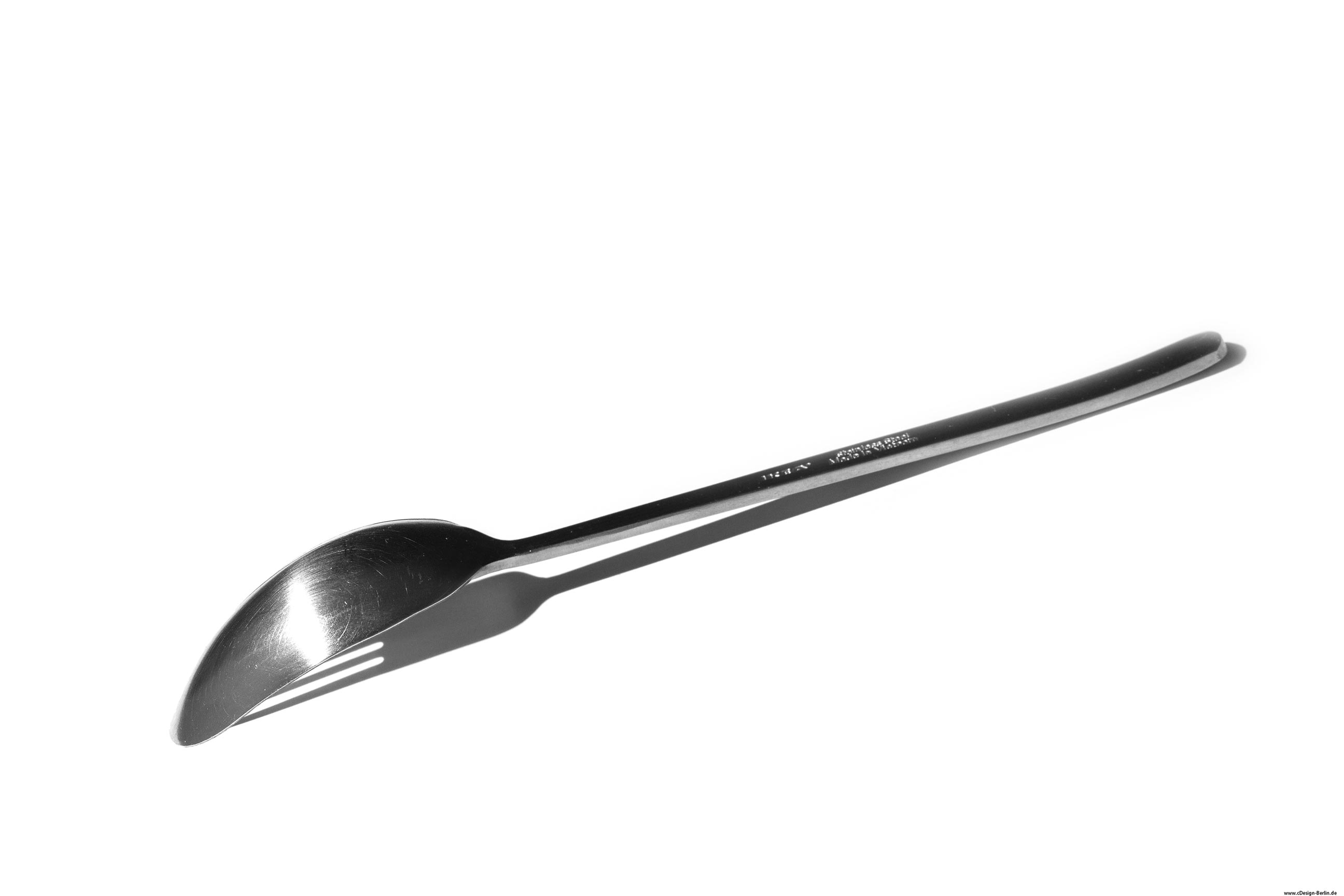 Auf diesem Foto ist ein Edelstahllöffel auf weißem Untergrund zu sehen. Das Licht ist so eingesetzt, das der Löffel einen Schatten werfen sollte, allerdings ist es nicht der Schatten des Löffels, sondern einer Gabel.