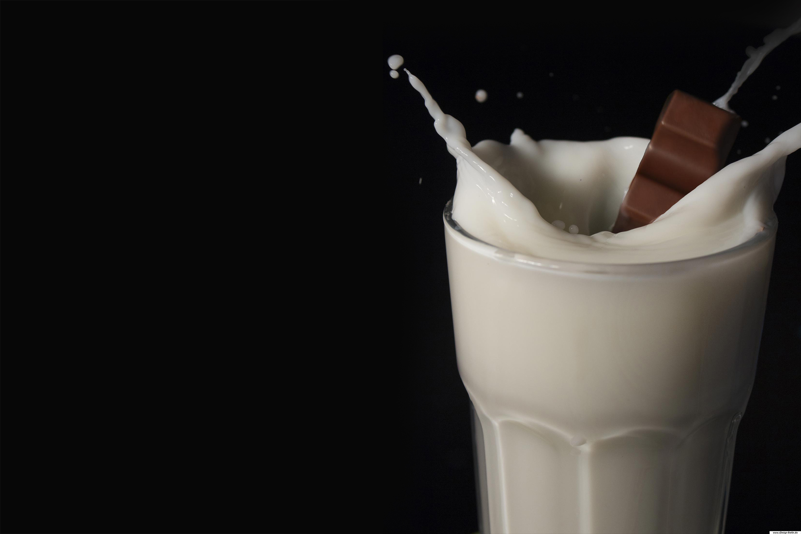 Der Hintergrund dieses Bildes ist schwarz und bildet einen starken Kontrast zu dem eigentlichen Motiv. Im Vordergrund sieht man ein Trinkglas, welches mit Milch gefüllt wurde. Ein Schokoriegel fällt in das mit Milch gefüllte Glas, so dass es von allen Seiten herausspritzt. Die einzelnen Spritzer sieht man scharf und diese Technik nennt man in der Fotografie Einfrieren. Dieser Prozess hat in einem Studio stattgefunden.