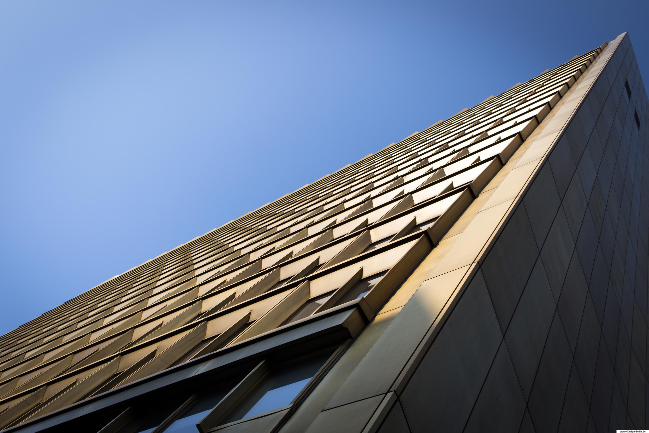 Berlin ist bekannt für seine unterschiedliche Architektur, denn kein Gebäude gleicht dem anderen. Dennoch findet jedes seinen eigenen Platz ohne deplaziert zu wirken. Es ist ein Zusammenspiel der verschiedenen Bauten und macht Berlin zu dem was es ist, einfach unverwechselbar. Vor mir steht das Gebäude des Axel-Springer-Verlages. Dieses Foto habe ich aus der Froschperspetive gemacht, um die Größe des Objektes zu unterstreichen. Die obere Spitze ragt in den strahlend blauen Himmel und schließt mit dem rechten oberen Bildrand ab. Die rechte Außenwand ist glatt und mit großen bräunlichen Kacheln versehen, welche sich überall wiederfinden. Die Hauptfläche des Gebäudes ist strukturiert, da Fenster in ihr eingebettet sind.